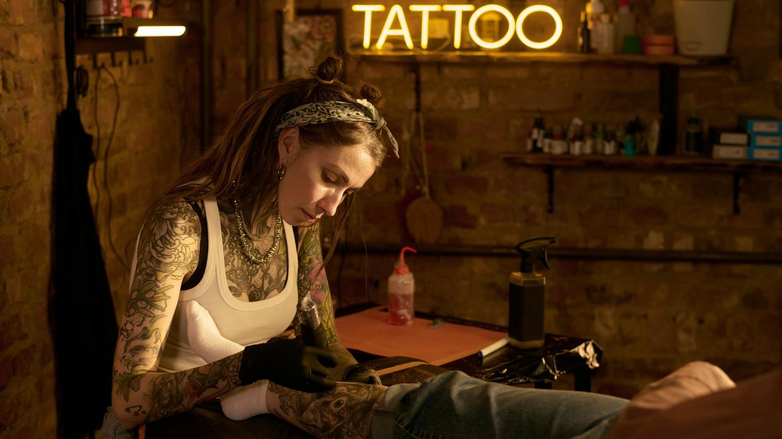 Tattoo-artiest zet geconcentreerd een tattoo onder een neonbord met het woord tattoo
