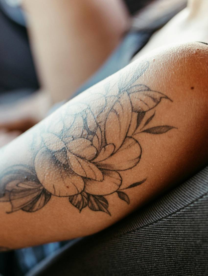 Fijnlijnige bloemtattoo met zachte grijstinten op een bovenarm